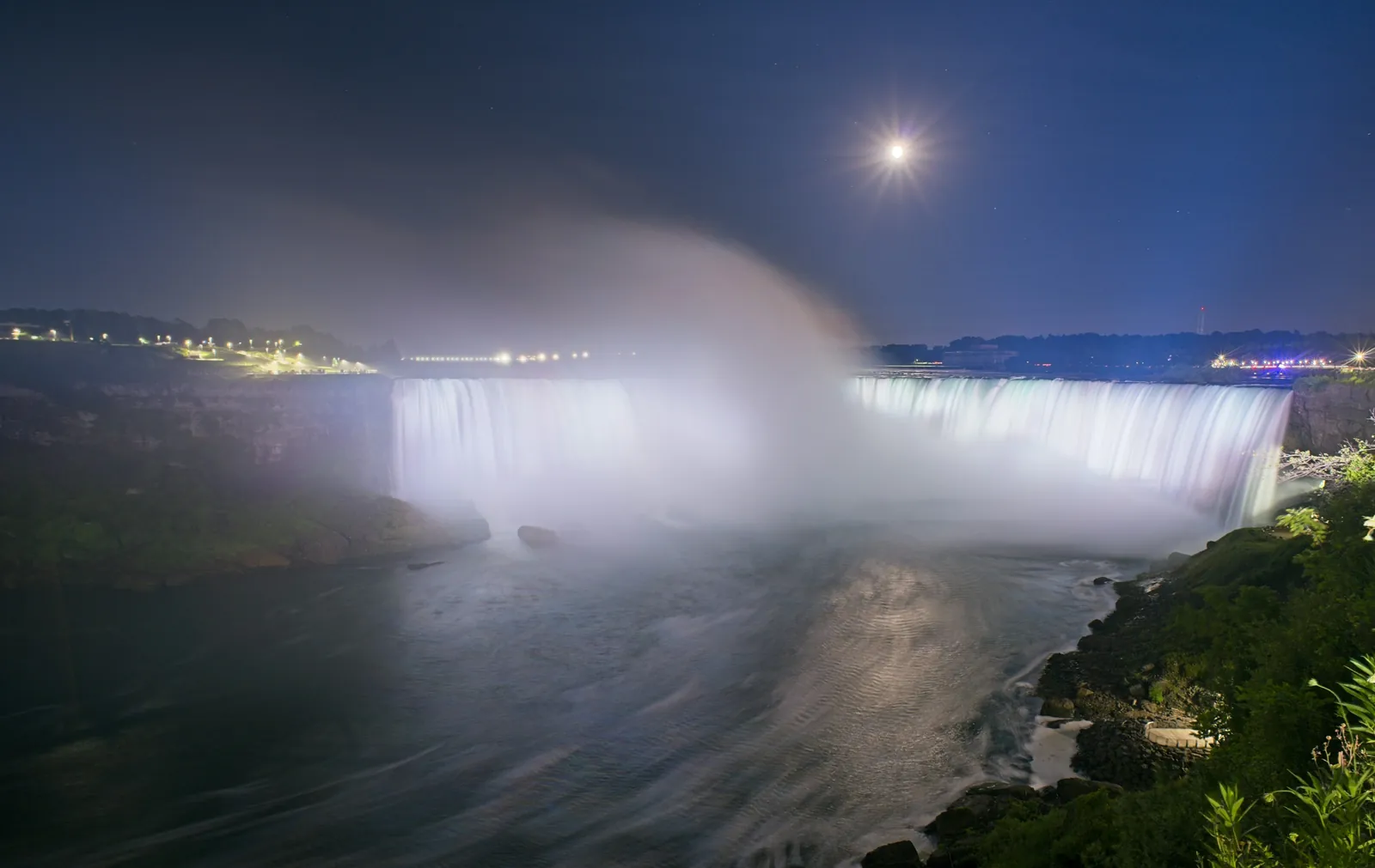 Horseshoe Falls, der gløder i flomlys under en klar måne, med en tågesøjle, der stiger op fra kløften mod en dybblå himmel